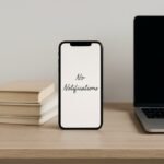 A minimalist wooden desk featuring a smartphone with a blank screen, stacked books, and a closed laptop, symbolizing digital minimalism and reduced notifications.